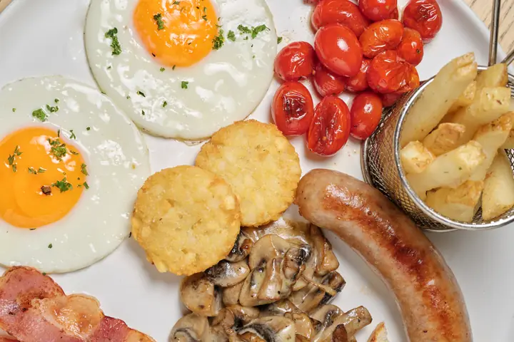 Breakfast plate with eggs, tomatoes, hash browns, chips, mushrooms, sausage, and bacon